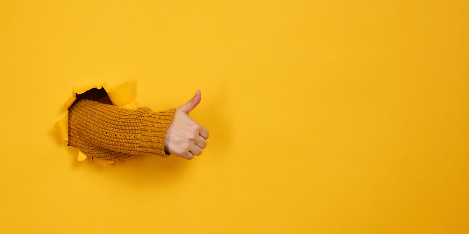 mano che spacca muro giallo ed esce facendo segno ok